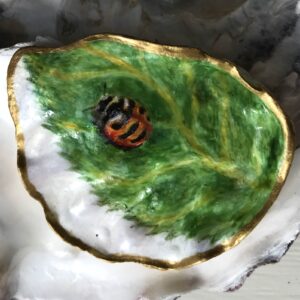 A tiny orange beetle with three black bands crawls up a birch leaf: all of it painted inside an oyster shell.