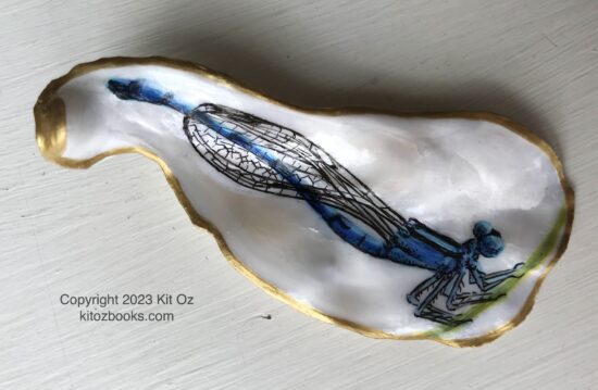 a thin blue damselfly painted inside a small, oblong oyster shell